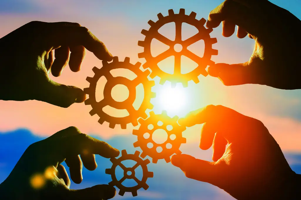 Četiri ruke drže zupčanike prema suncu, dobro uvezani, tim, zajedništvo